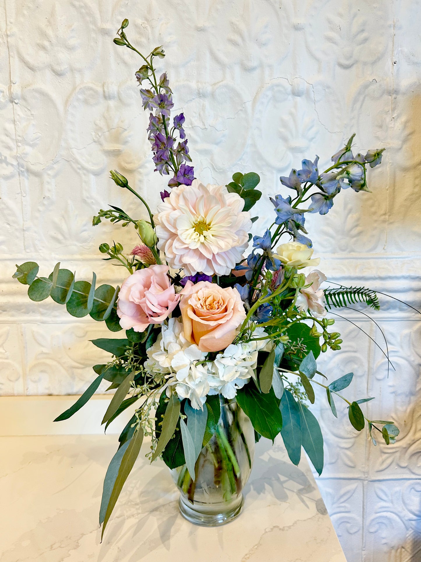Bouquet of flowers in a clear vase against a textured white wall.