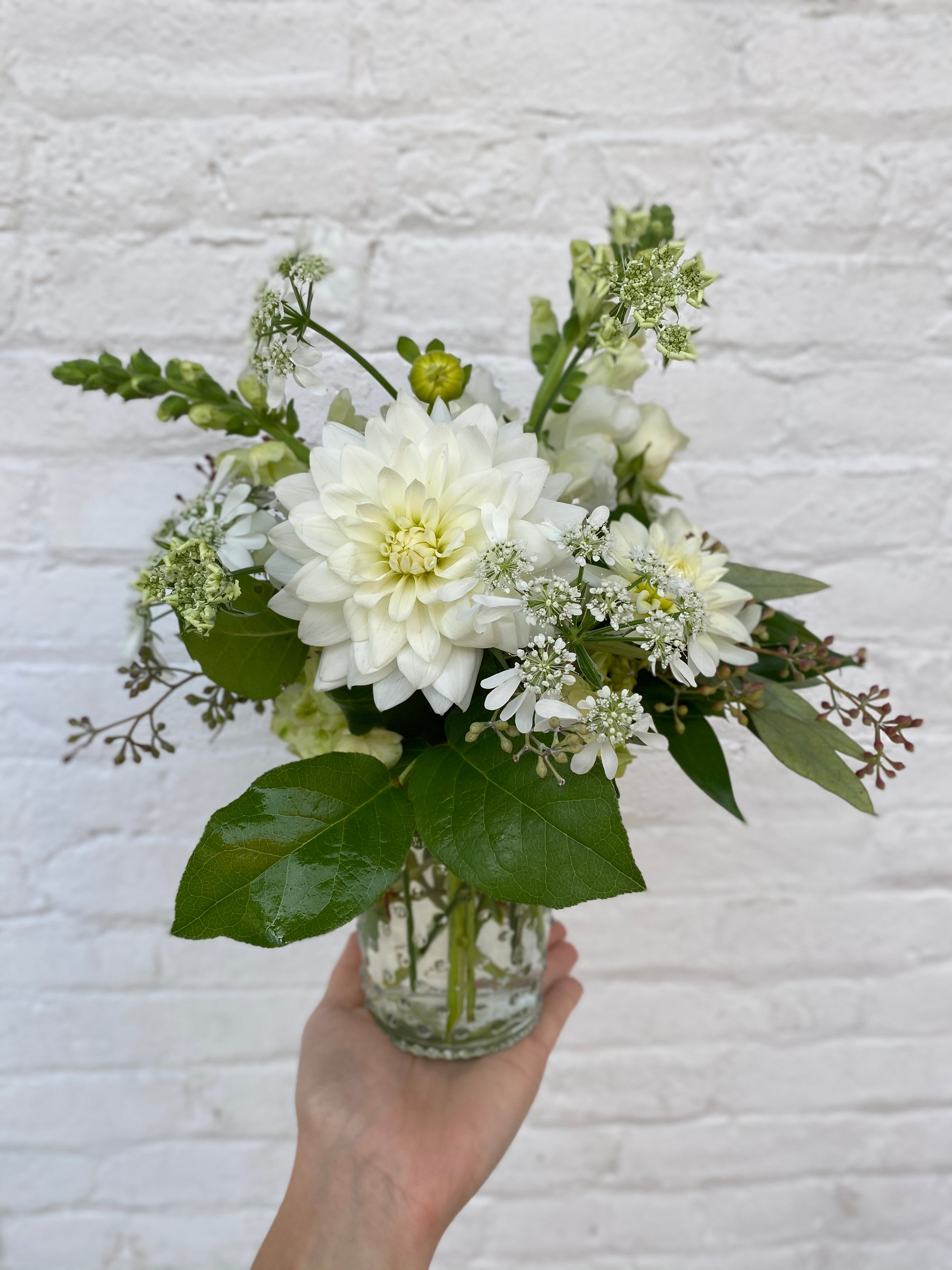 Bouquet of white flowers in a clear vase held against a textured white background