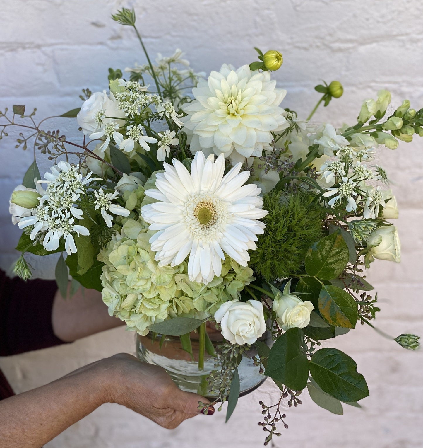 Bouquet of white and green flowers held by a person against a neutral background