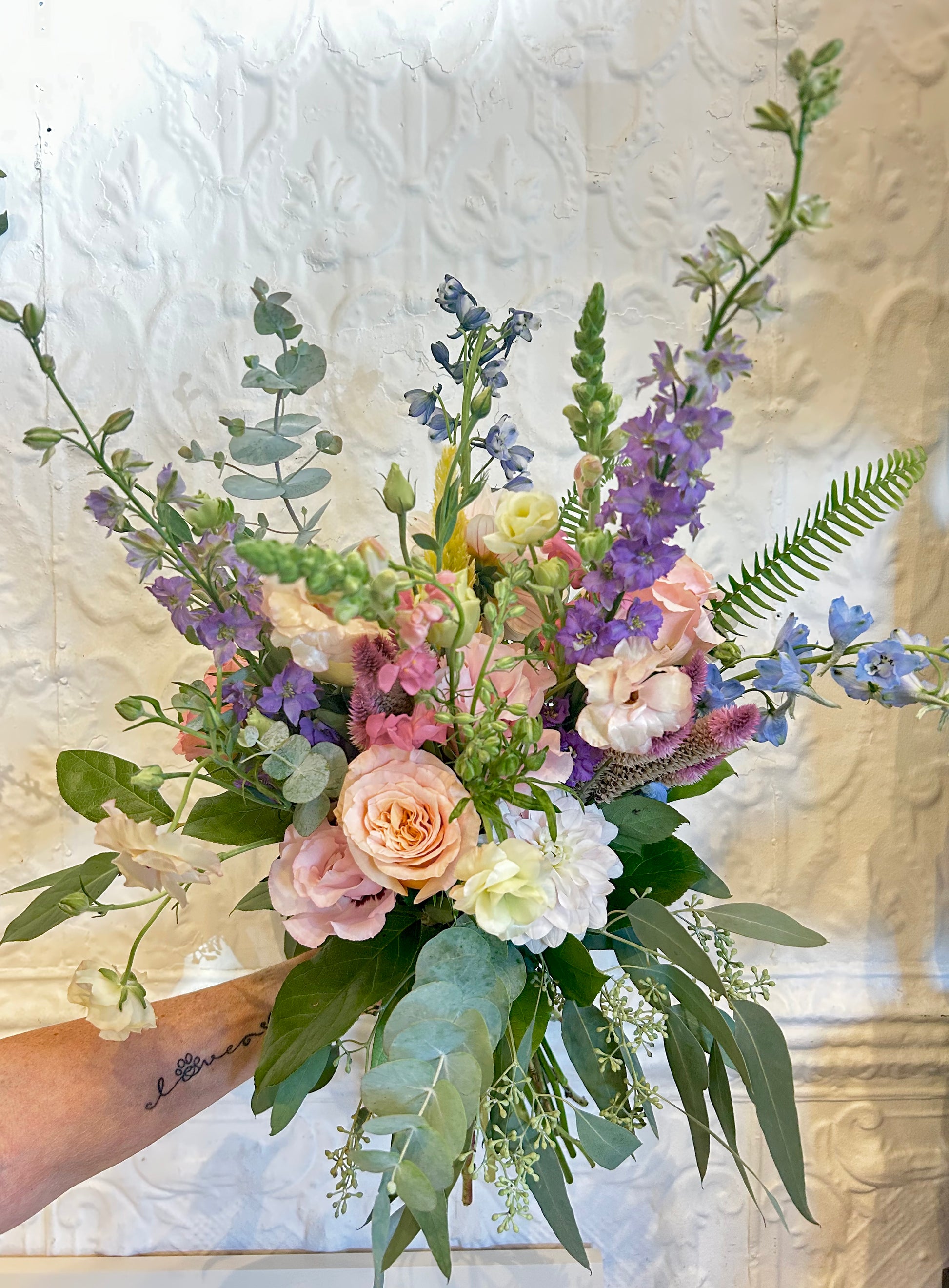 Bouquet of flowers held by a person against a textured white wall.