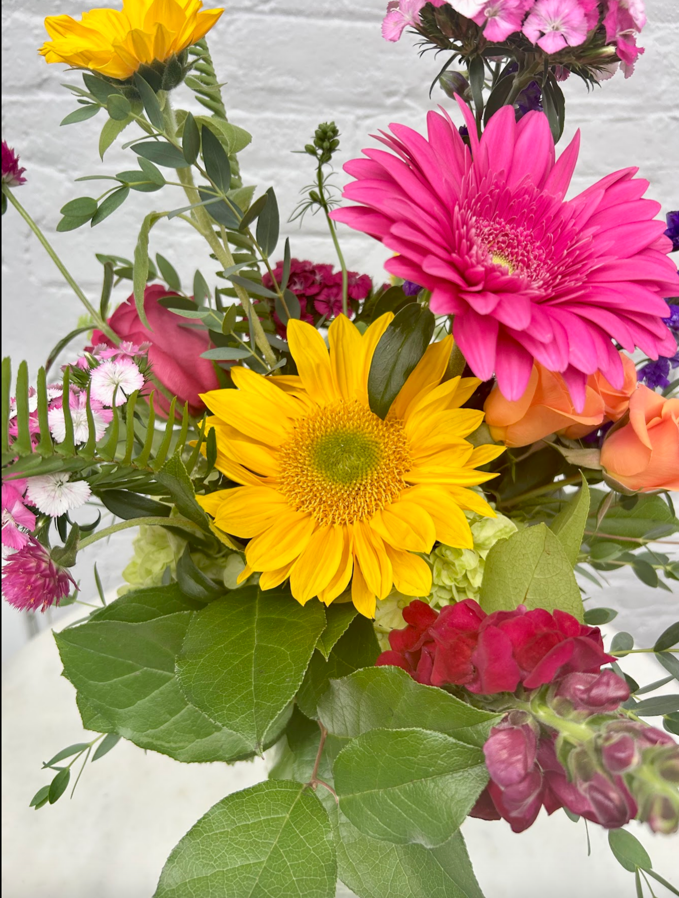 Bouquet of colorful flowers including a yellow daisy and pink gerbera with green leaves on a light background.