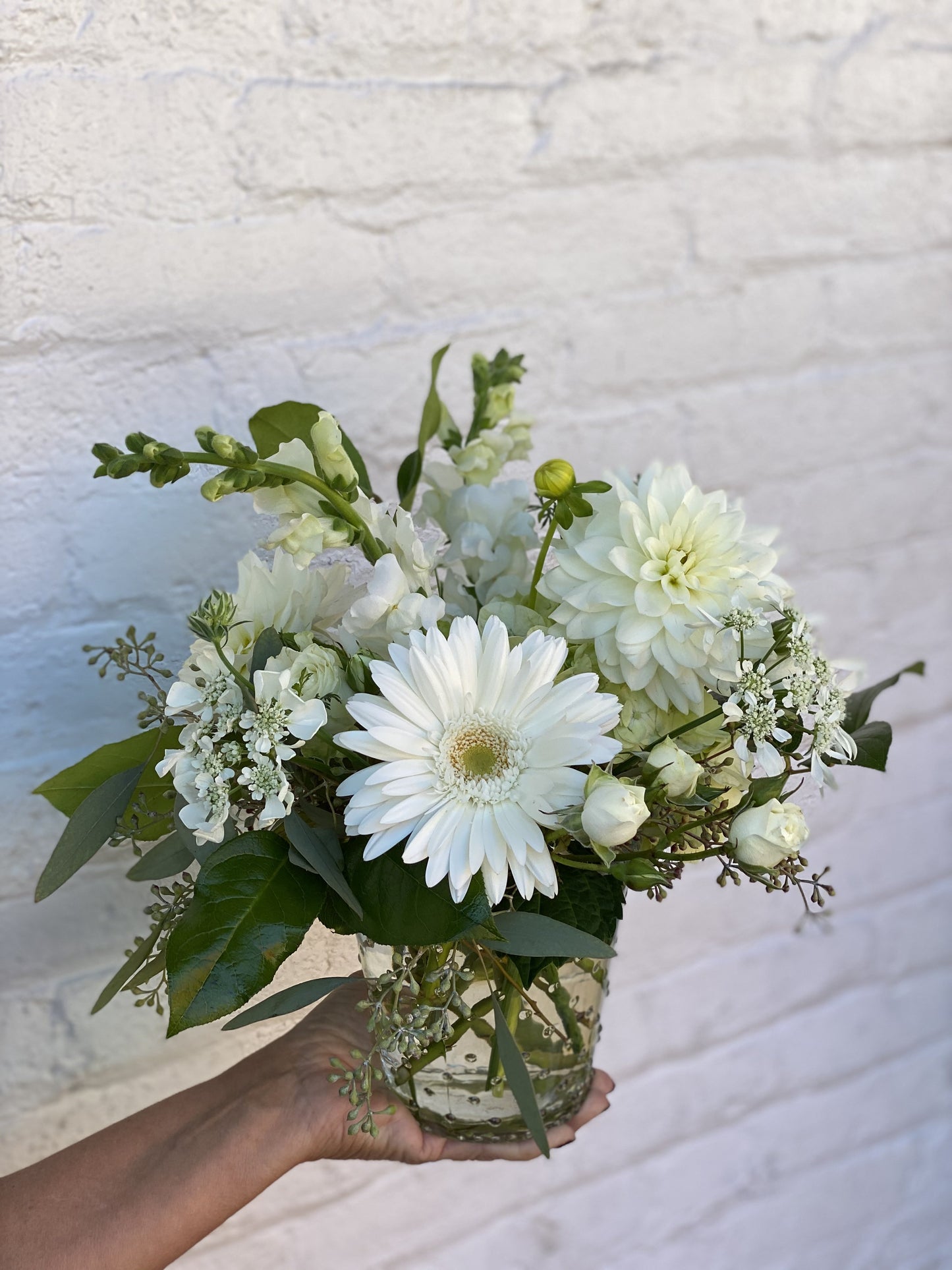 Bouquet of white flowers held by a hand against a light textured background