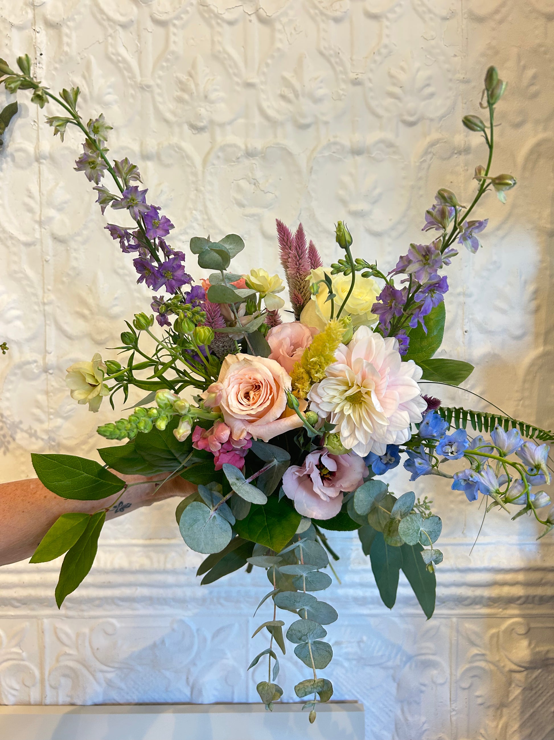 Bouquet of flowers held against a textured white wall